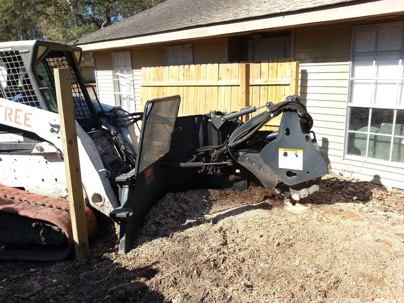 Skid steer with a stump grinder attachment beside a house